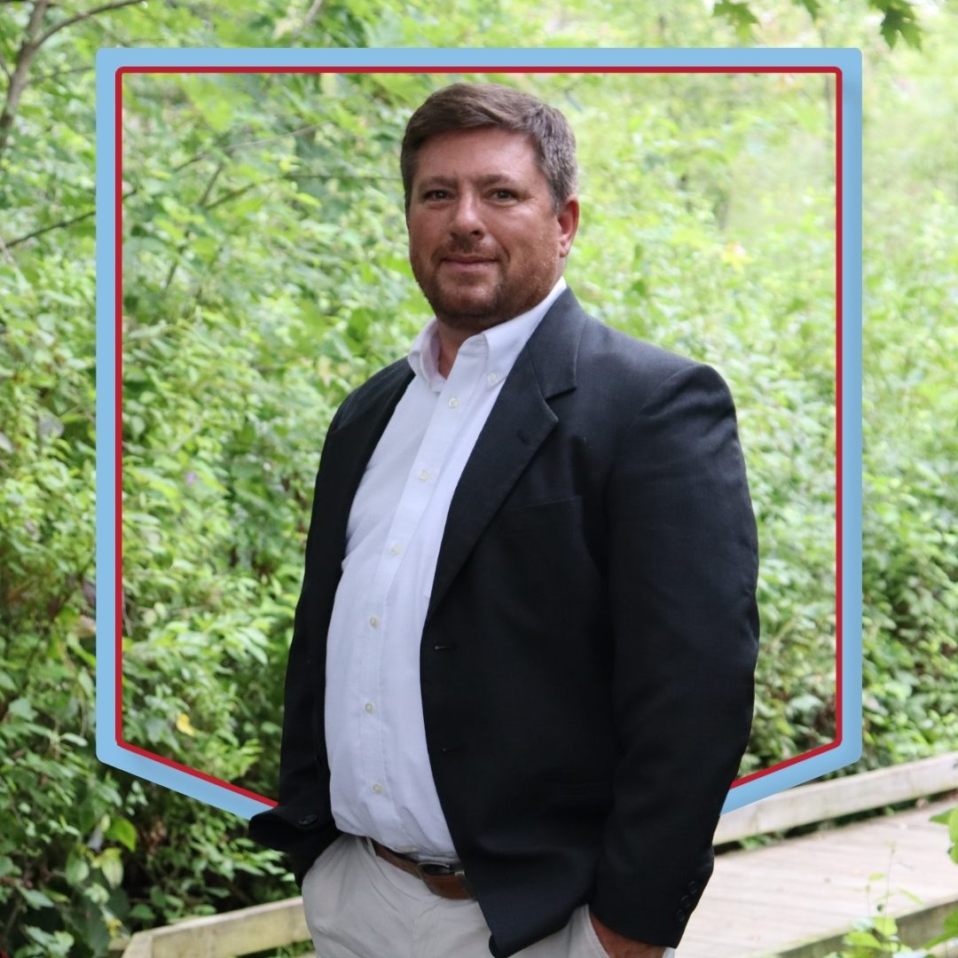 Sam Plew poses in front of a wooded background.